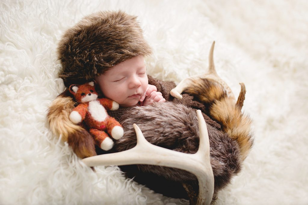 Newborn baby boy wearing a coonskin cap with a stuffed fox and elk antlers