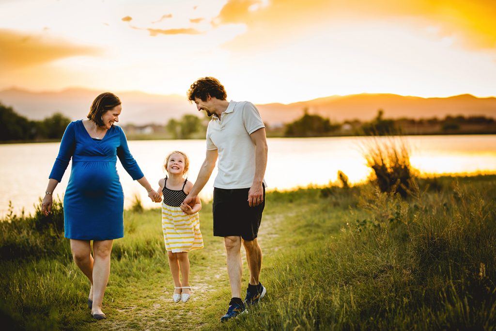 A family of three walks together by the lake during their maternity photo session in Loveland Colorado