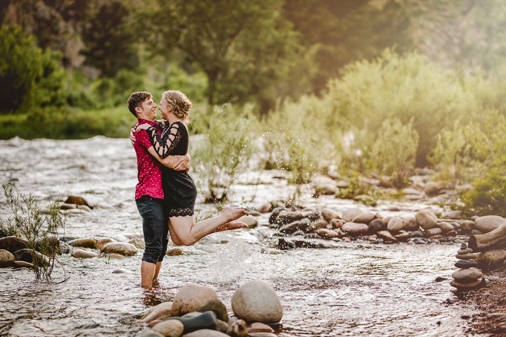A couple plays in the Poudre River during their engagement photo shoot at Picnic Rock in Northern Colorado