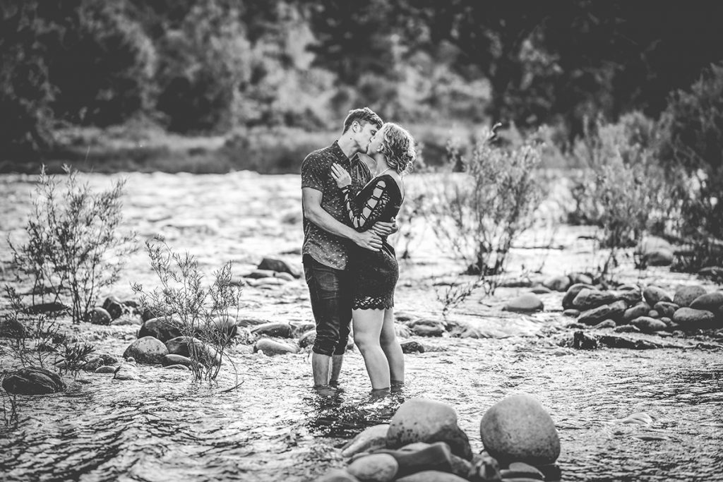 Black and white photo of a couple kissing while they stand in the river in Fort Collins, Colorado