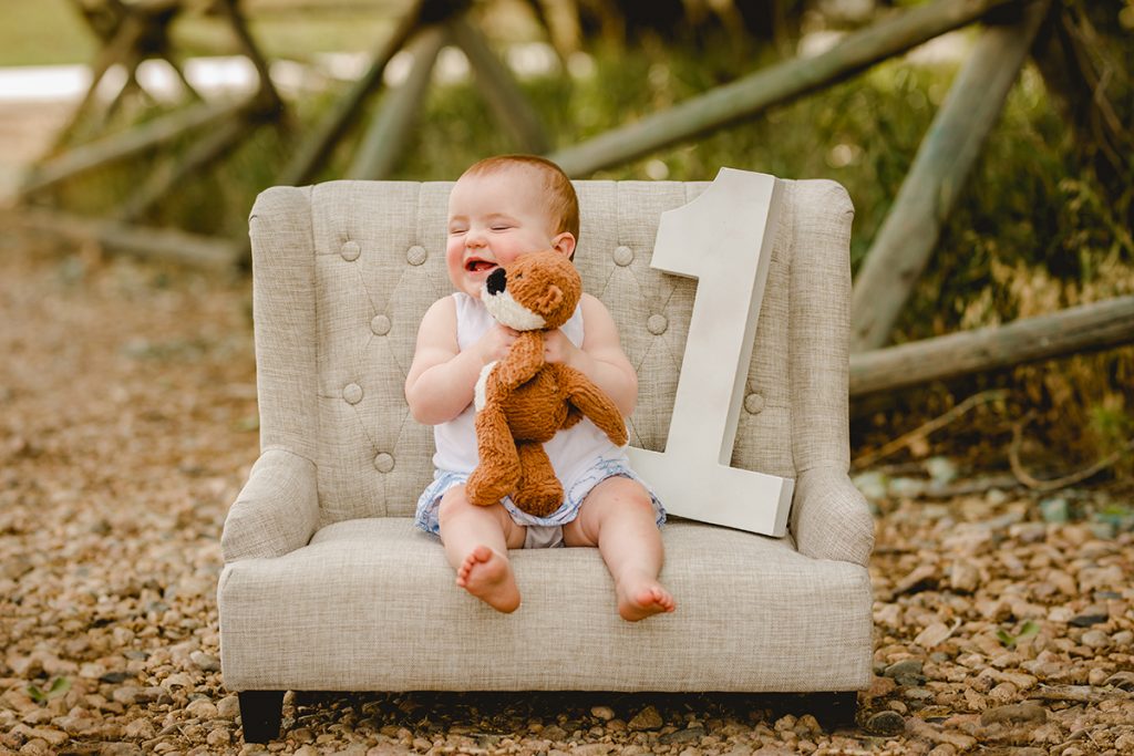 Baby girl hugs her stuffed animal while she sits on a little couch in a photo taken by Becky Michaud, FOrt Collins Baby Photographer