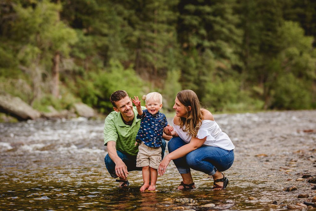 A little boy plays in the river with his parents during their photography session on the poudre river