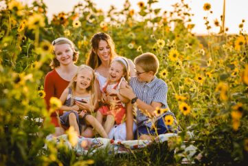 A family laughs and plays together in a sunflower field in a photo taken by Becky Michaud, Fort Collins photographer