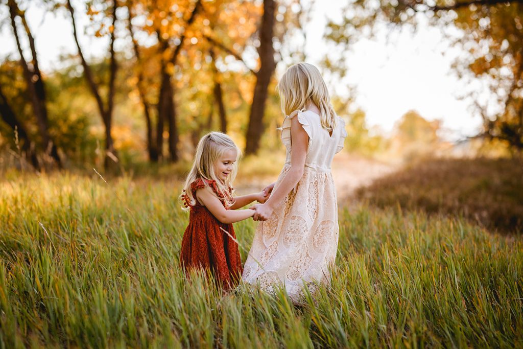 Two little girls in lace dresses play in a field together in Fort Collins