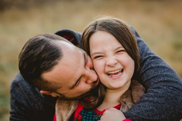 A dad kisses his laughing daughter's cheek