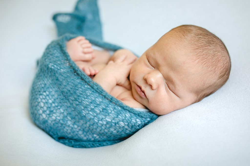 Newborn baby boy wrapped up in a blue knit blanket for his Fort Collins newborn photography session
