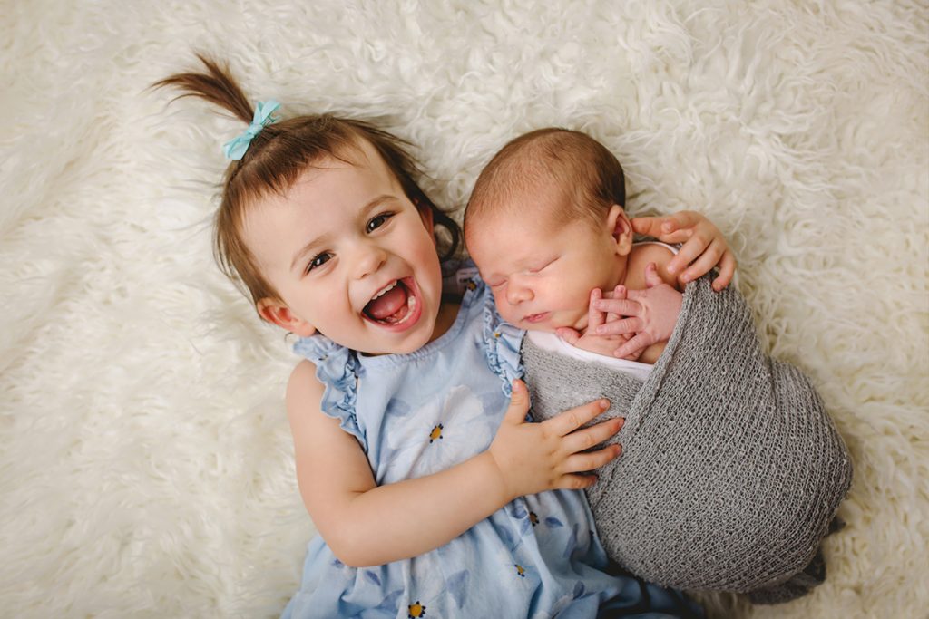 A little girl smiles as she holds her brother during his newborn photo session in their Fort Collins home