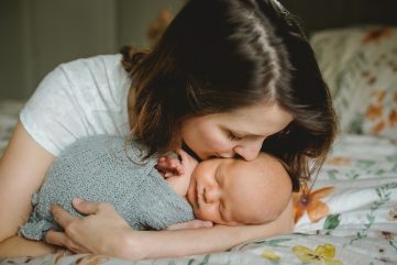 Mom kisses baby's cheek during his in home newborn photo session in Colorado