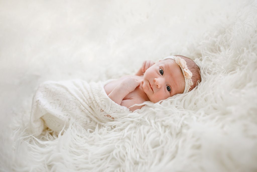 Bright eyed baby looks at the camera during her newborn photography session in her Northern Colorado home