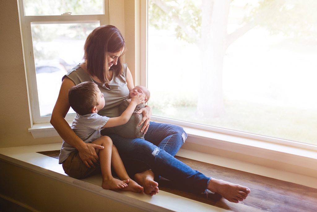 Mom and her two boys snuggle together on a window seat during their Fort Collins lifestyle newborn photography session