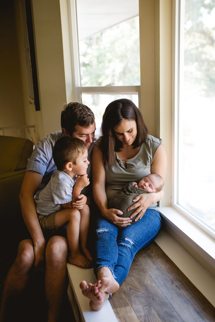 Lifestyle newborn photo in Fort Collins home with family sitting in bay window