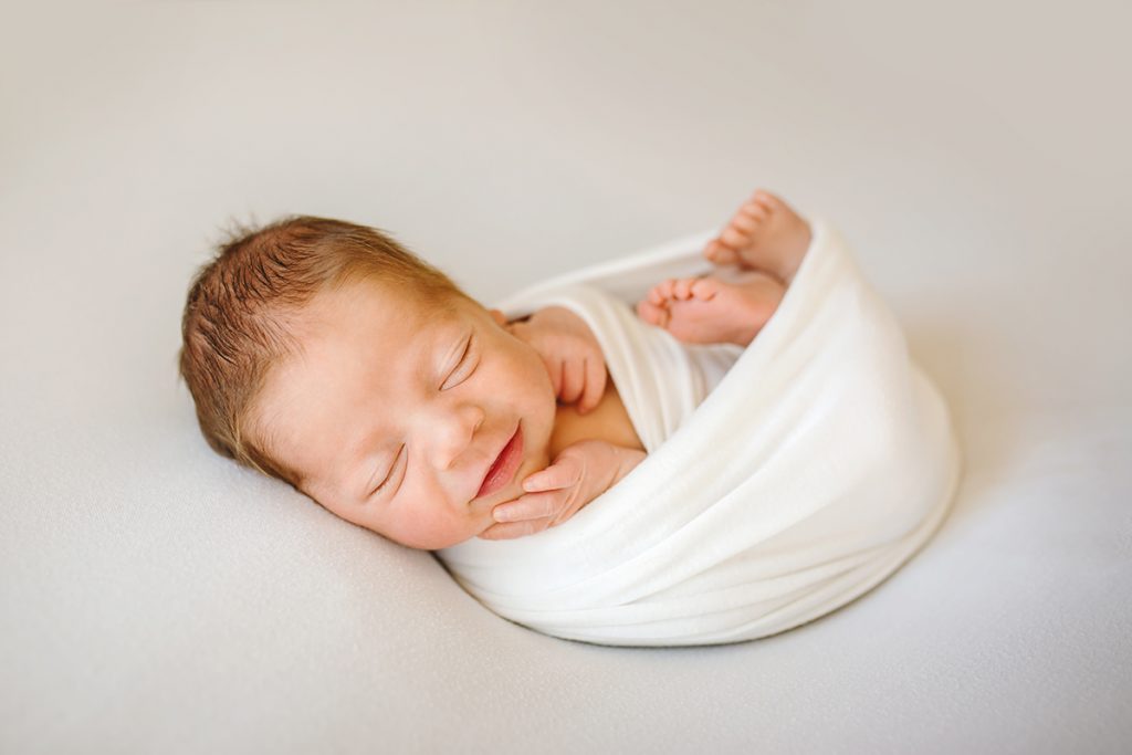 Photo of a smiling newborn on white taken by Becky Michaud, Colorado newborn photographer