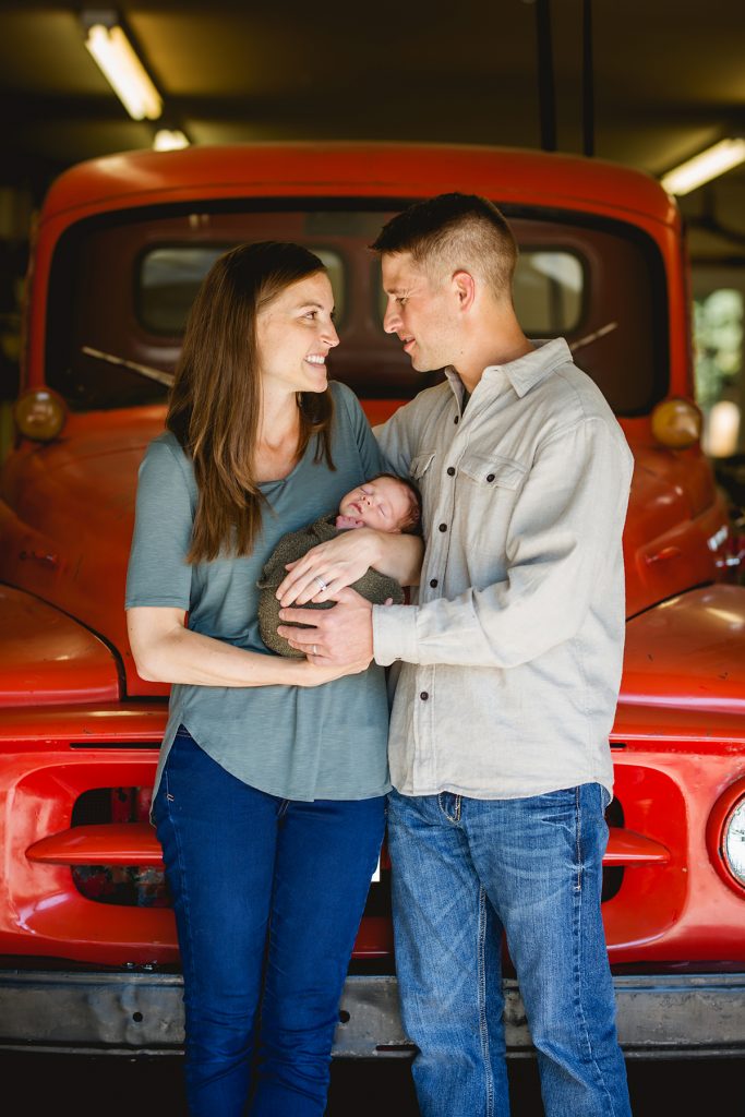 A couple poses in front of their vintage truck with their newborn baby boy