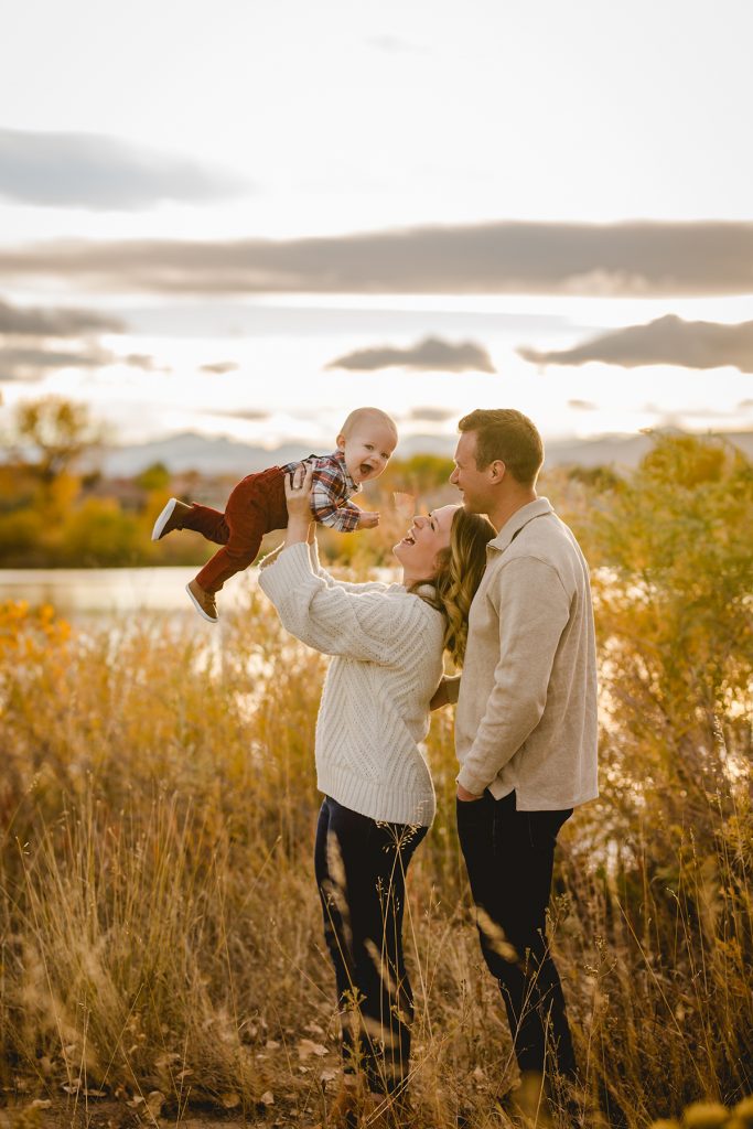 mom and dad play with their baby boy during his one year old photo shoot by a lake in Colorado