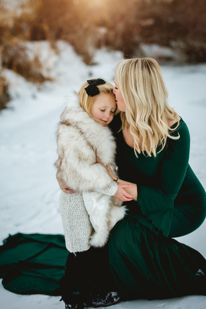 mom kisses daughter in the snow in a photo taken by Becky Michaud, Fort Collins photographer