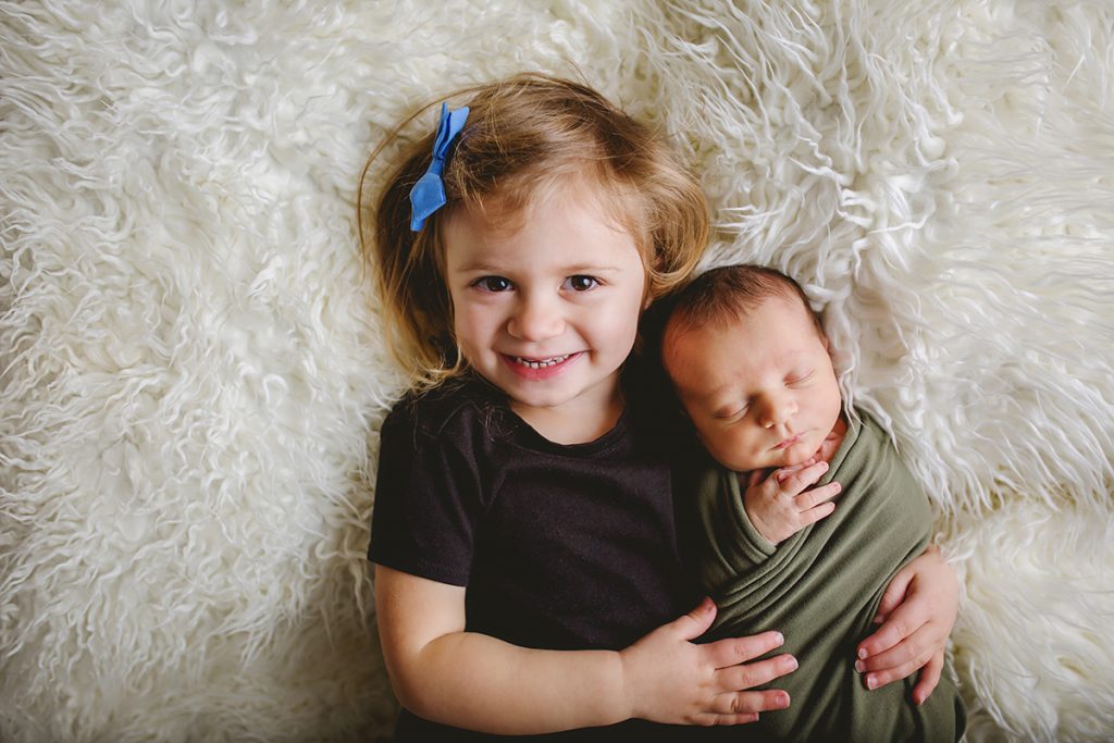 A little girl holds her baby brother in a photo taken during his newborn photography session in Northern Colorado