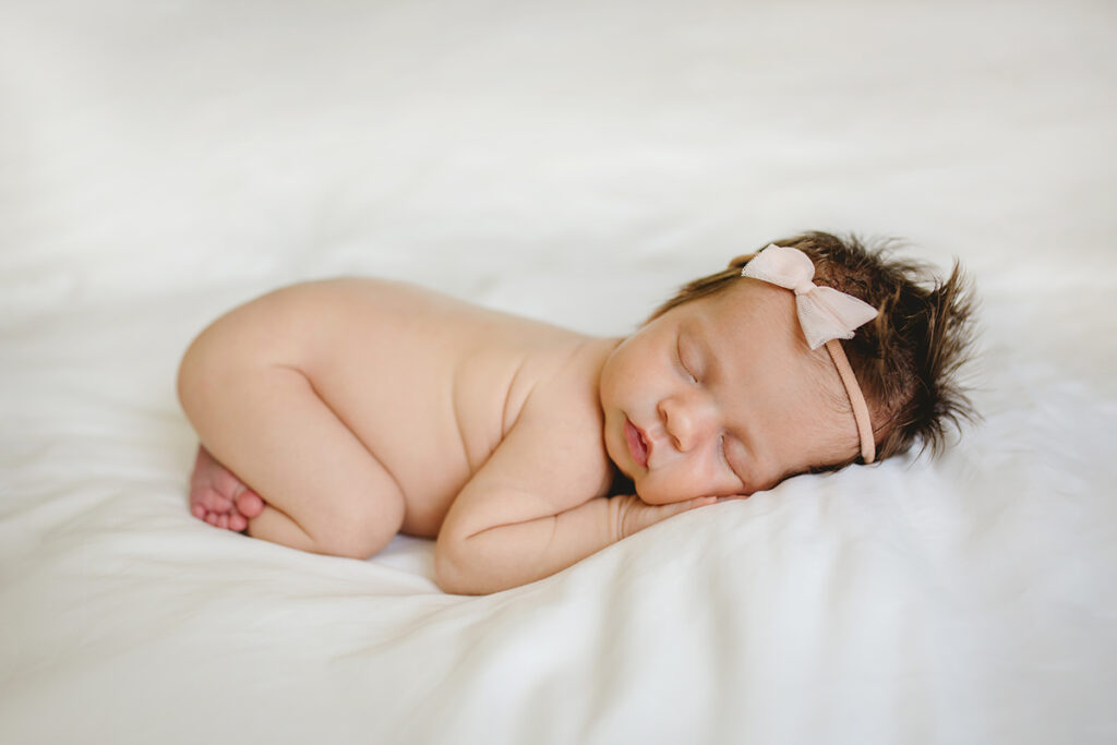 Simple photo of a newborn baby girl on white with a pink bow taken by Becky Michaud, Fort Collins baby photographer