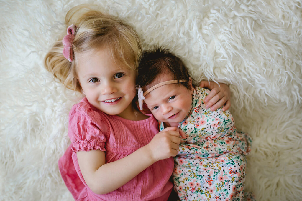 A little girl poses with her baby sister during their newborn photography session in their Fort Collins home